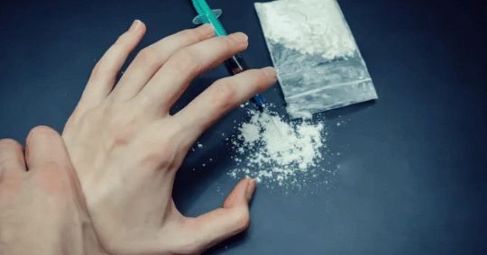 A person grabbing the hand of someone reaching out for a package of drugs. (Photo: iStock/Yaraslau Mikheyeu)